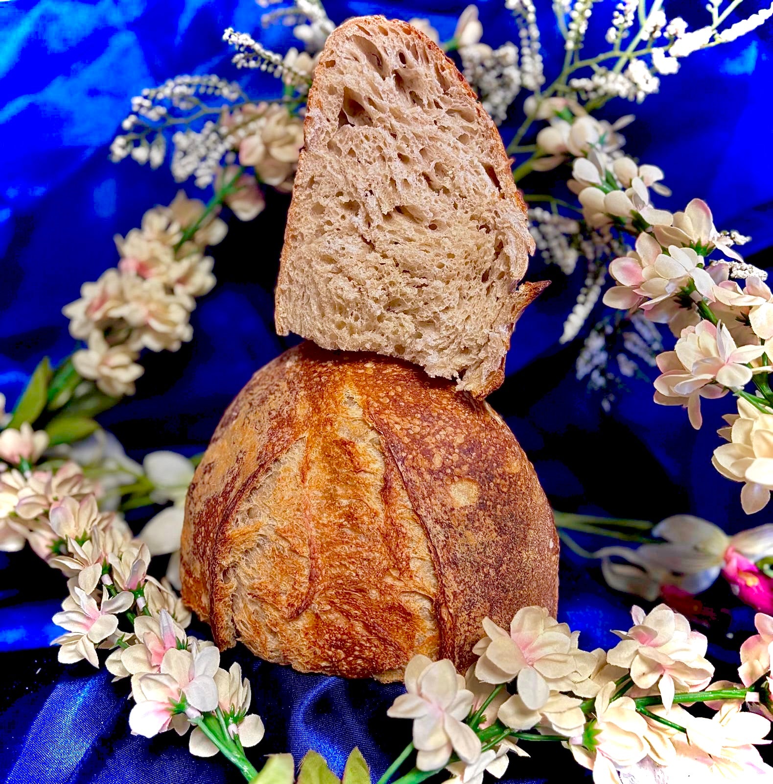 Loaf of bread with a slice on top, surrounded by flowers on a blue background