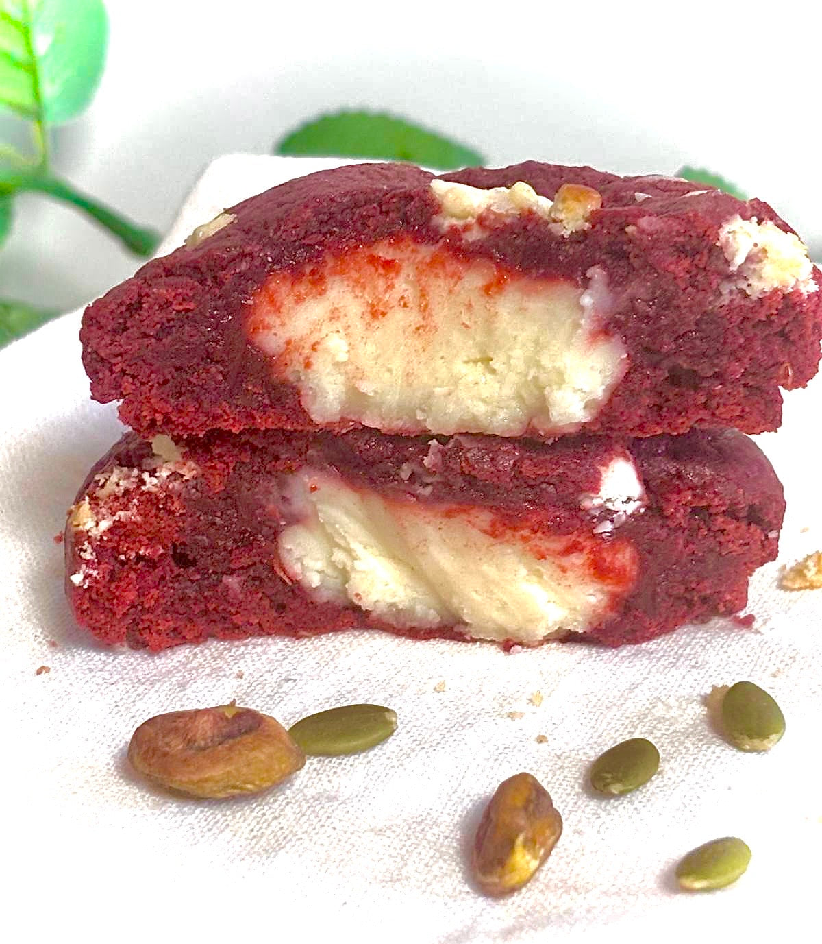 Red velvet cookie with cream cheese filling on a white surface with seeds around